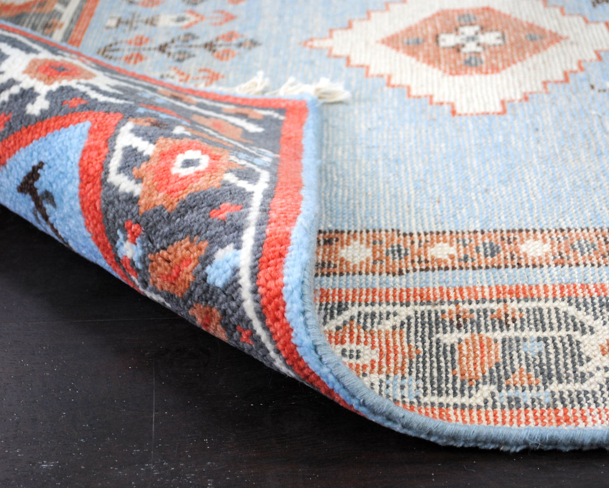Nilgiri hand-knotted rug folded back to show the wool pile and the knotted reverse side by side, with the bound side edge, Art Avenue