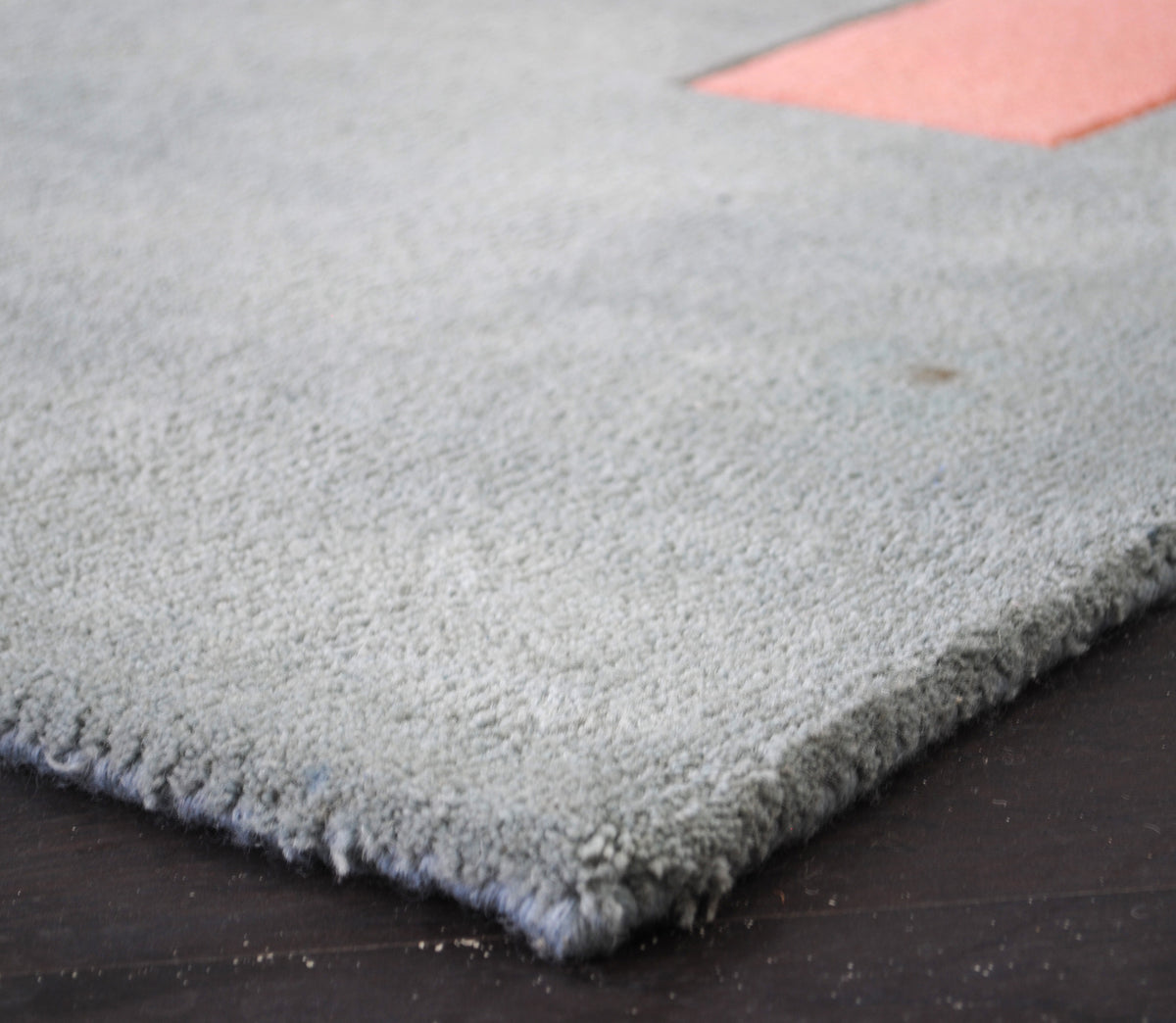 Close-up of the Pondicherry rug's dense cut wool pile at the edge, sea-glass blue with the coral bar beyond, hand-tufted New Zealand wool, Art Avenue