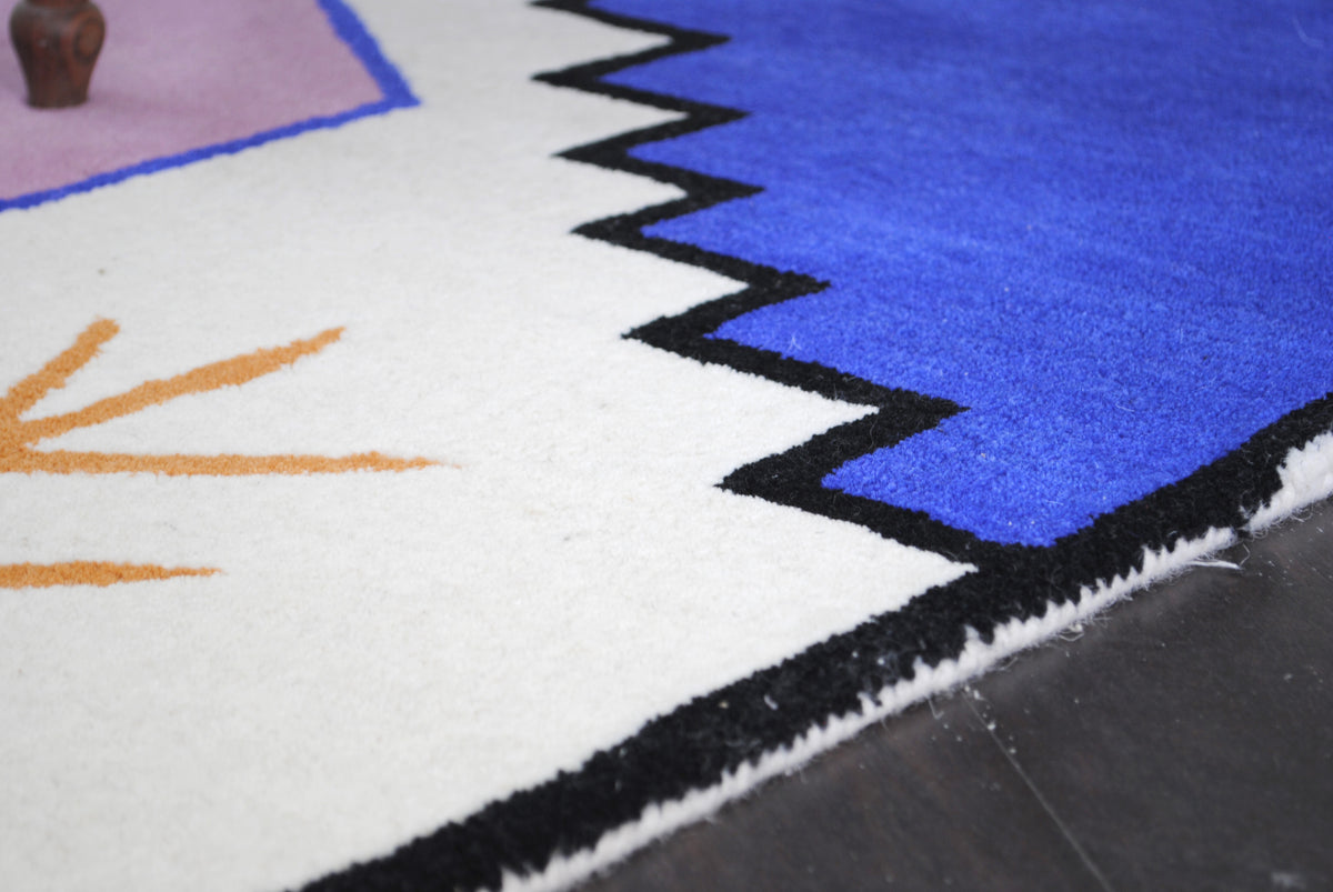 Close view of the Hampi rug's zigzag black outline between the ivory ground and cobalt field, and the wool-bound edge, hand-tufted New Zealand wool, Art Avenue