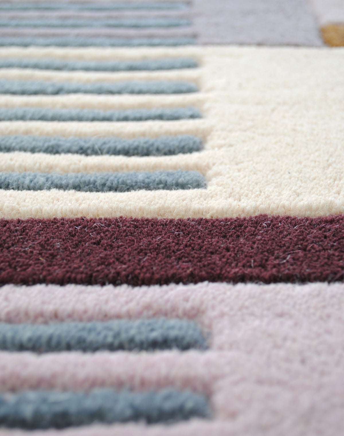 Macro view of the Mumbai rug's hand-tufted wool pile: teal stripes, an ivory block and an aubergine bar separated by carved channels, Art Avenue