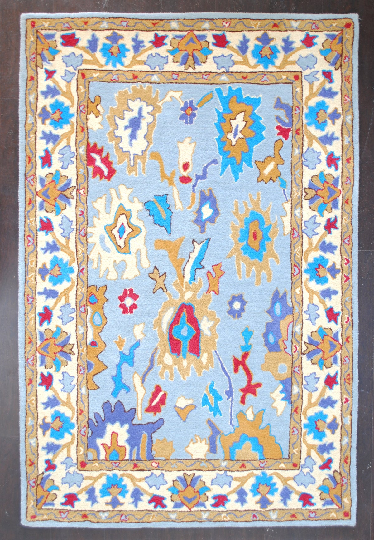Agra hand-tufted rug, full overhead view: scattered Mughal-style palmettes on a sky-blue field with an ivory floral border