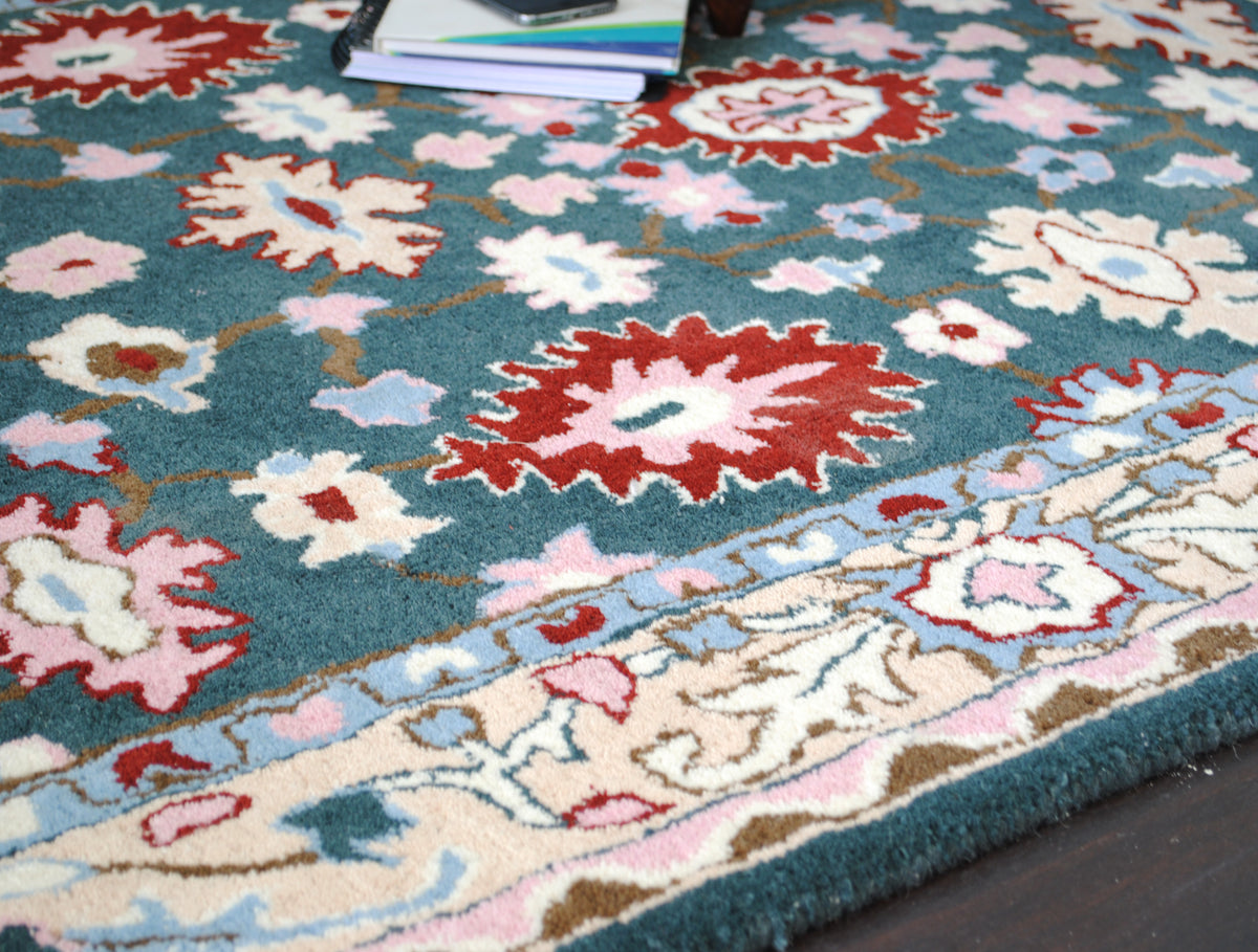 Srinagar hand-tufted rug, angled view of the teal floral field meeting the cream vine border and sky-blue guard stripe