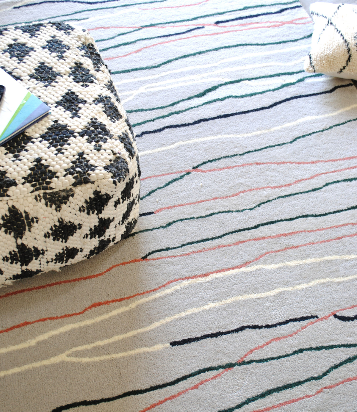 Looking down at the Chilika rug: rose, green, navy and ivory lines crossing a soft grey wool field