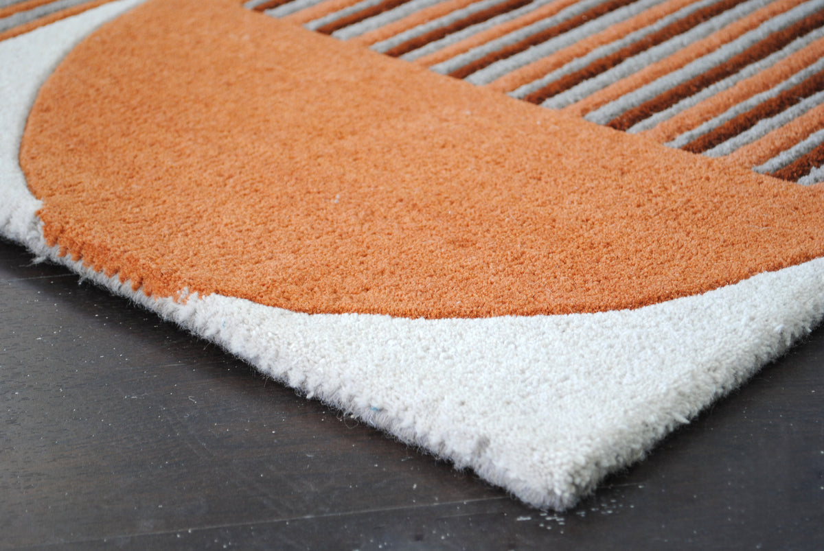 Corner of the Ahmedabad rug with a burnt orange half-circle and grey wool-bound edge, no fringe