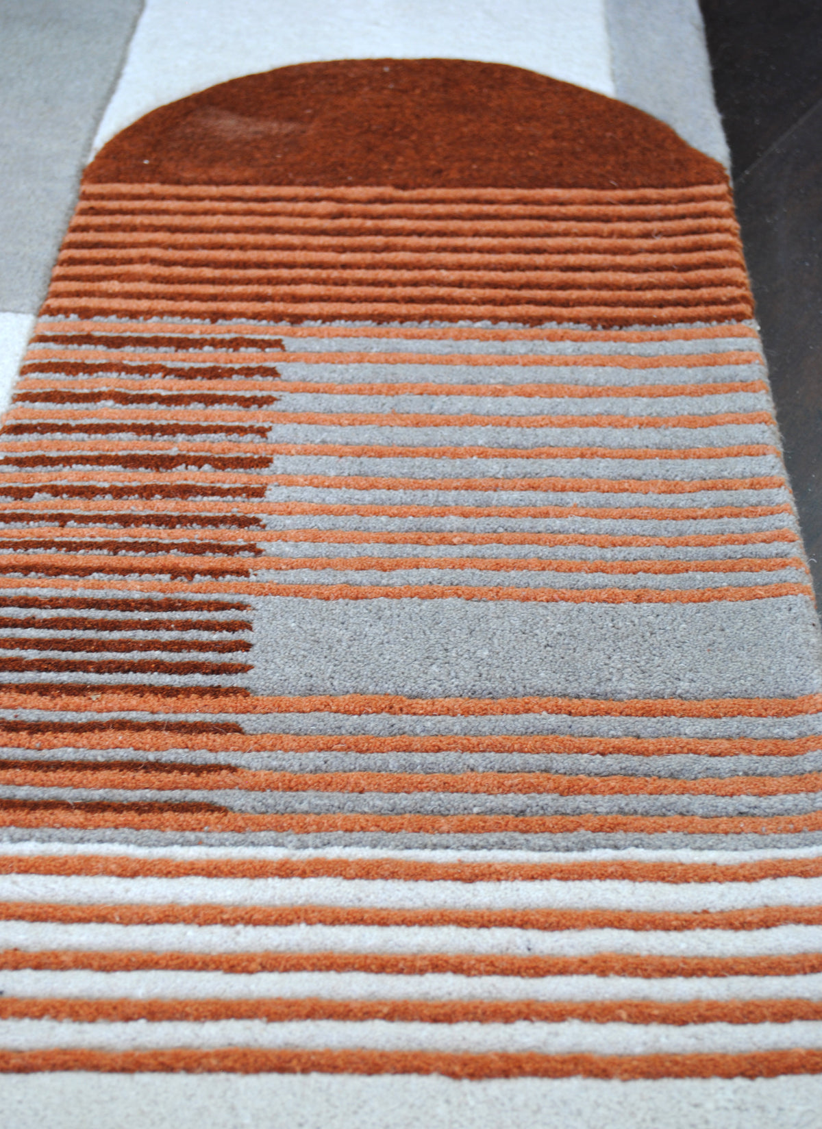 Close-up of a rust arch above striped terracotta and grey bands on the Ahmedabad wool rug