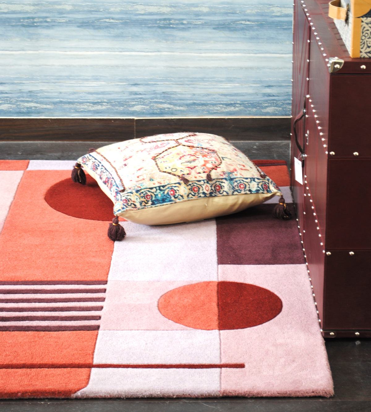 Konark geometric wool rug on a dark wood floor with a printed cushion and a studded trunk