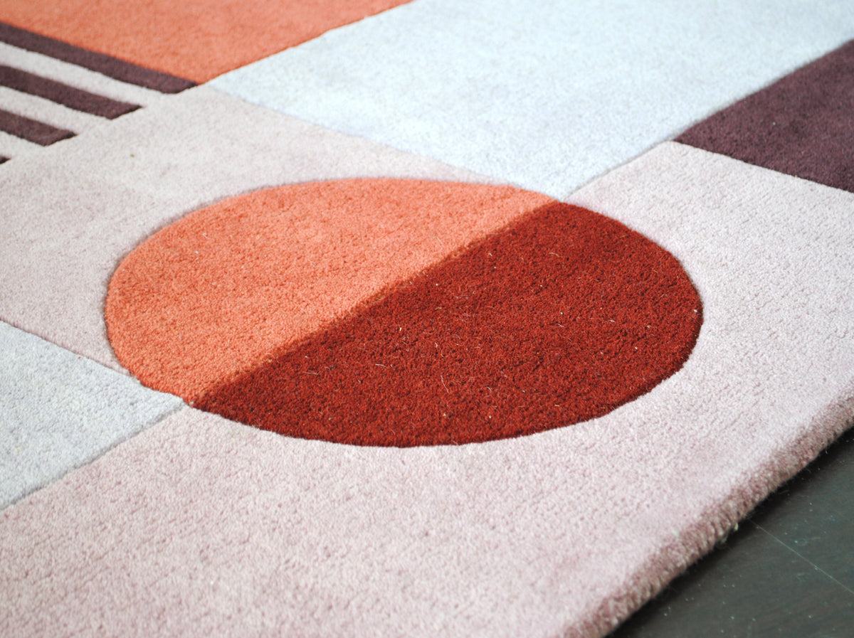 Close-up of a split sun-disc in terracotta and rust set into blush pink and plum panels on the Konark rug