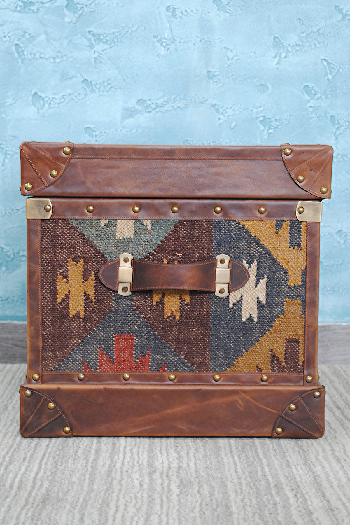 End face of the Madras kilim trunk with its stitched leather carry handle on brass mounts