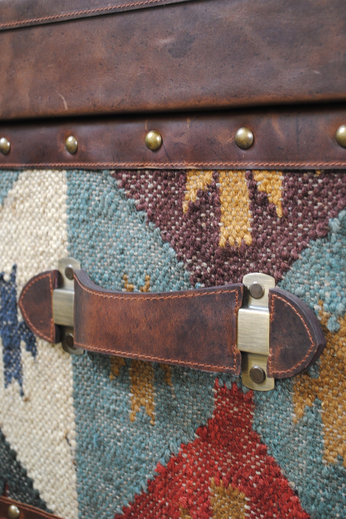 Close-up of the leather carry handle and antique brass mounts on the Madras kilim trunk