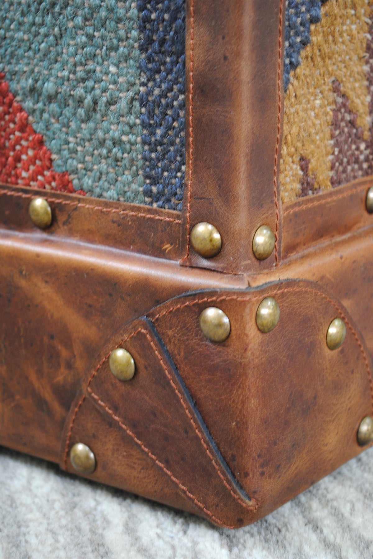 Base corner detail of the Madras kilim trunk showing saddle stitching and hand-set brass studs