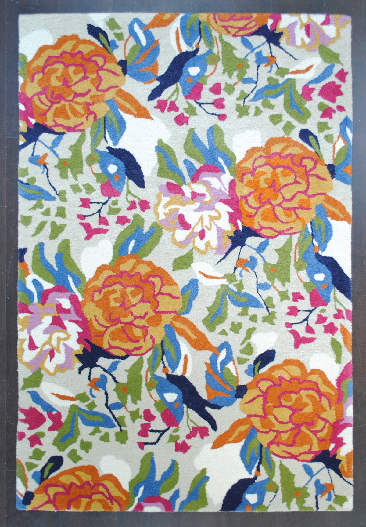 Ooty hand-tufted rug, full overhead view on a dark floor: orange peonies, fuchsia buds, navy birds and olive foliage on a pale grey ground, 4×6 ft