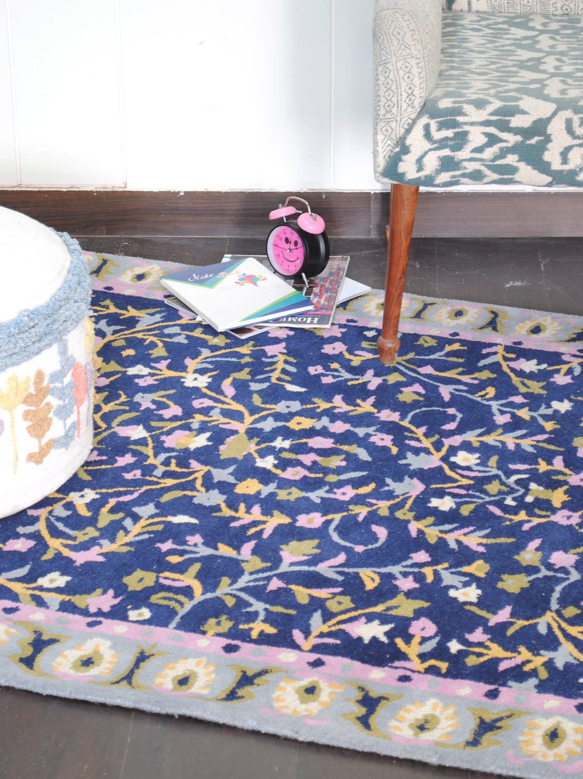 Nishat navy floral rug beneath an ikat armchair and a white pouf on a dark wood floor