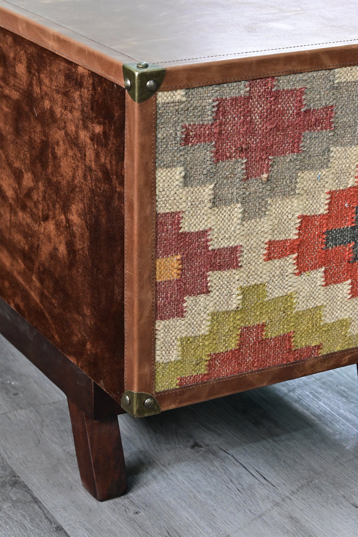 Rear corner of the Ranakpur TV unit, suede-finished back meeting the kilim flank at a brass corner cap