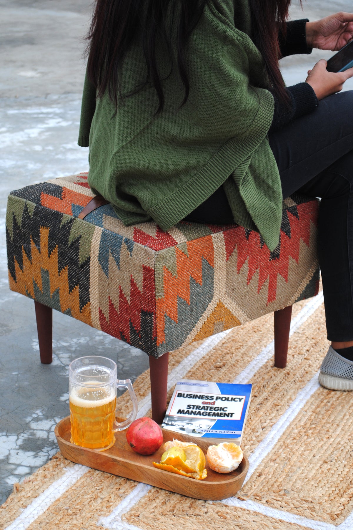 Ajanta kilim ottoman seating a person, with a serving tray on the jute rug alongside
