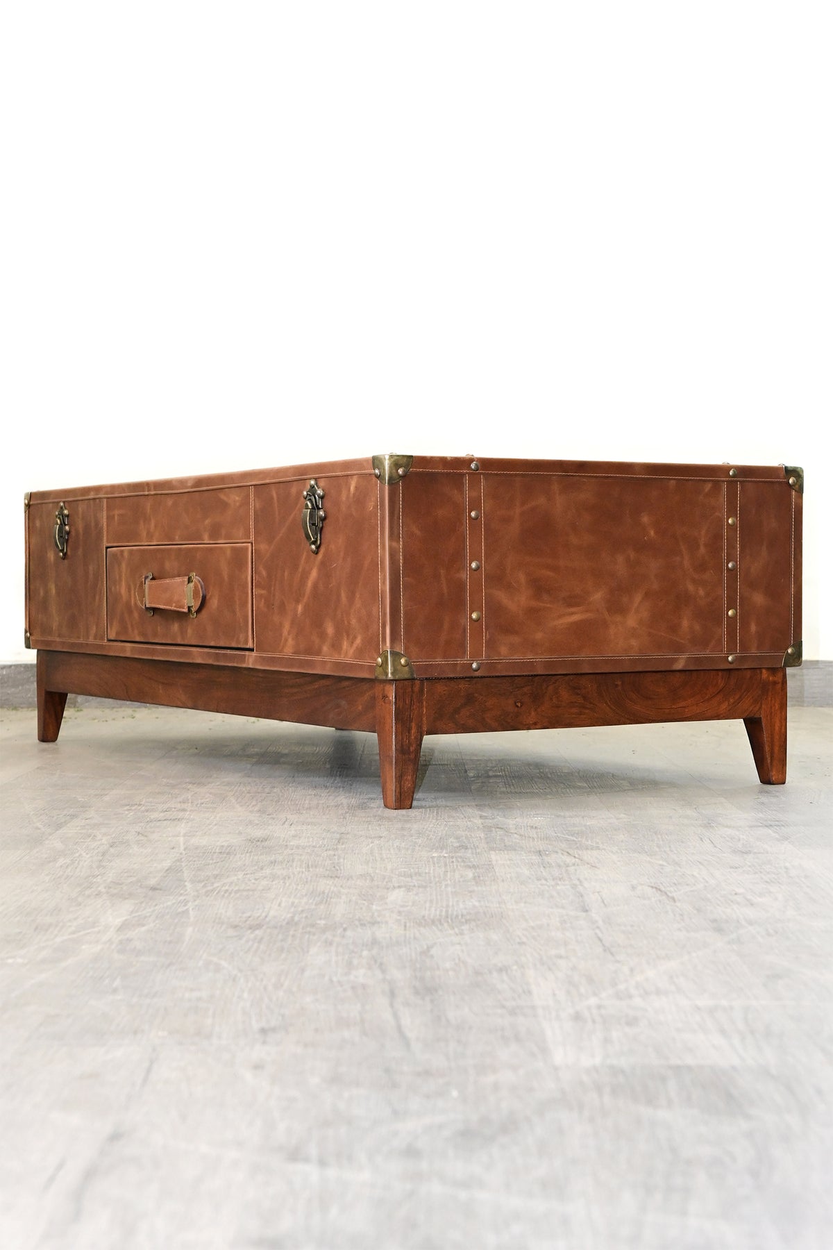 Kuchaman leather trunk coffee table, low three-quarter view showing the studded end panel and solid wood plinth