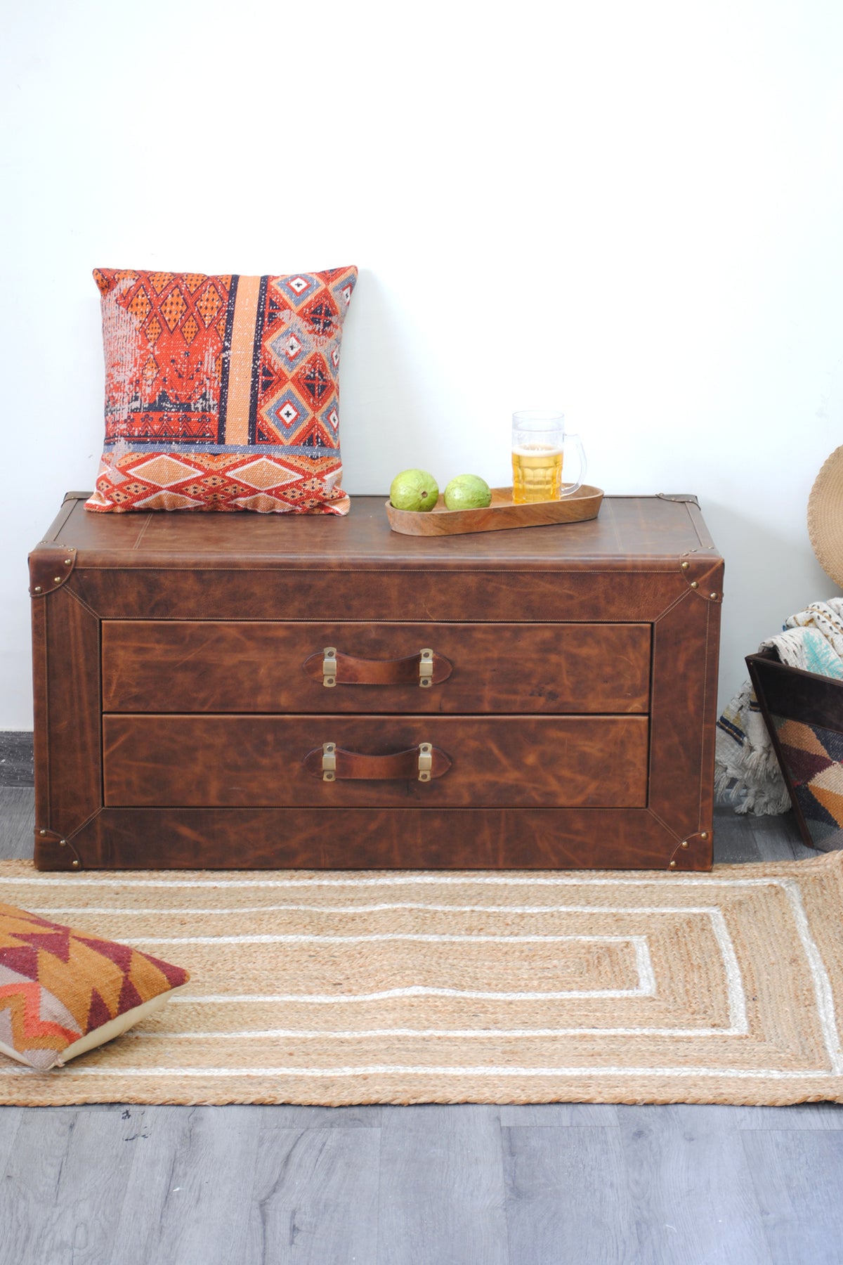 Deogarh leather drawer trunk against a white wall with a kilim cushion and a wooden serving tray