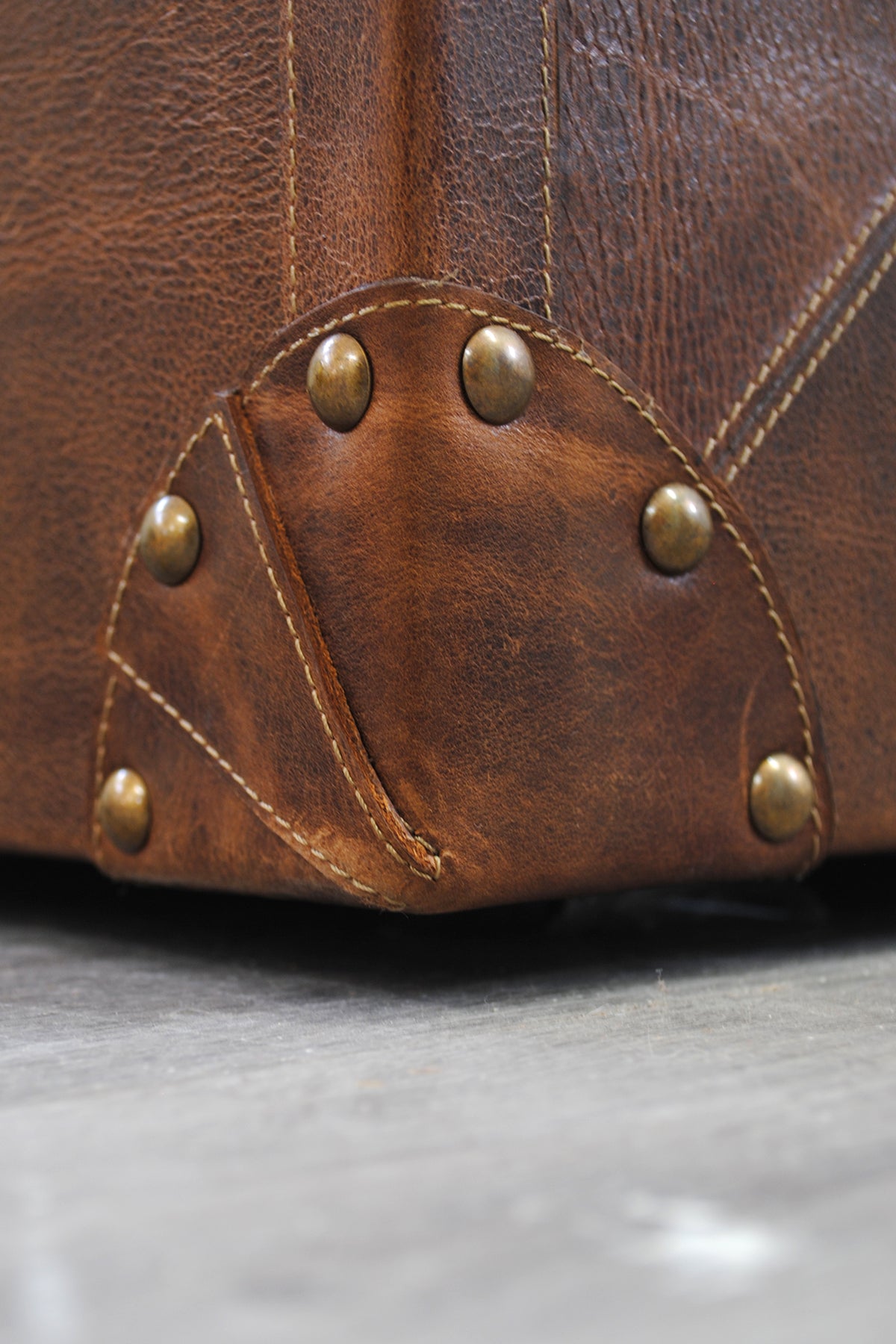 Macro detail of a riveted brass corner cap and hand-stitched leather seam