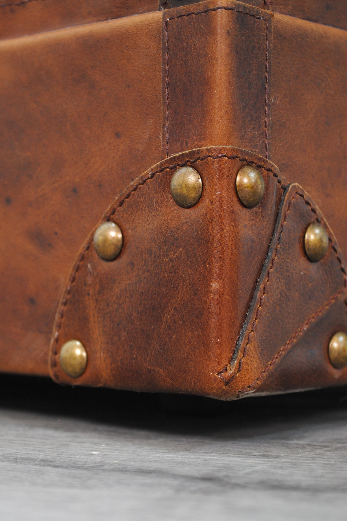 Macro detail of a riveted leather corner cap and domed brass studs on the Bundi trunk
