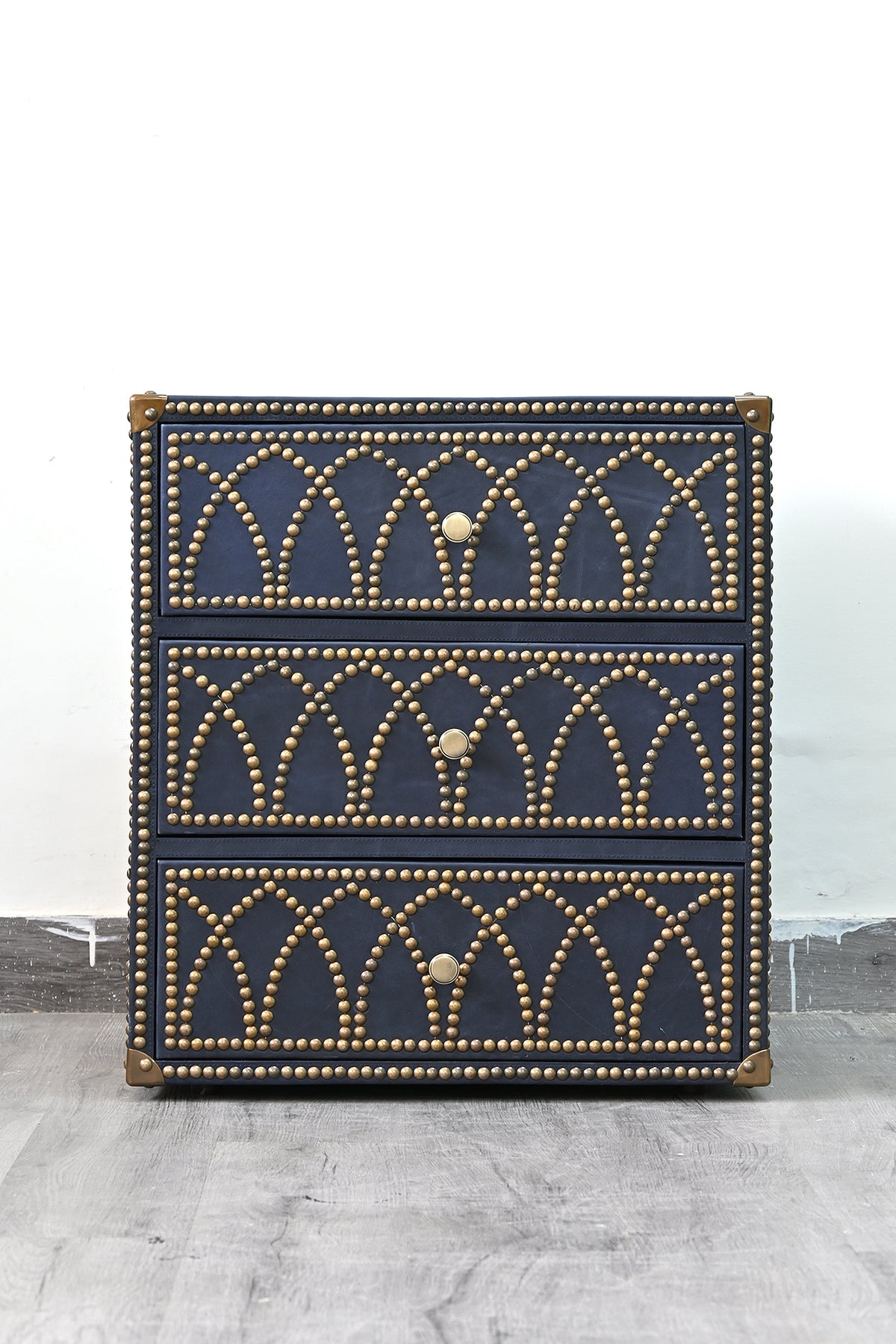 Front elevation of the Samode bedside chest with three drawers in brass-studded navy leather
