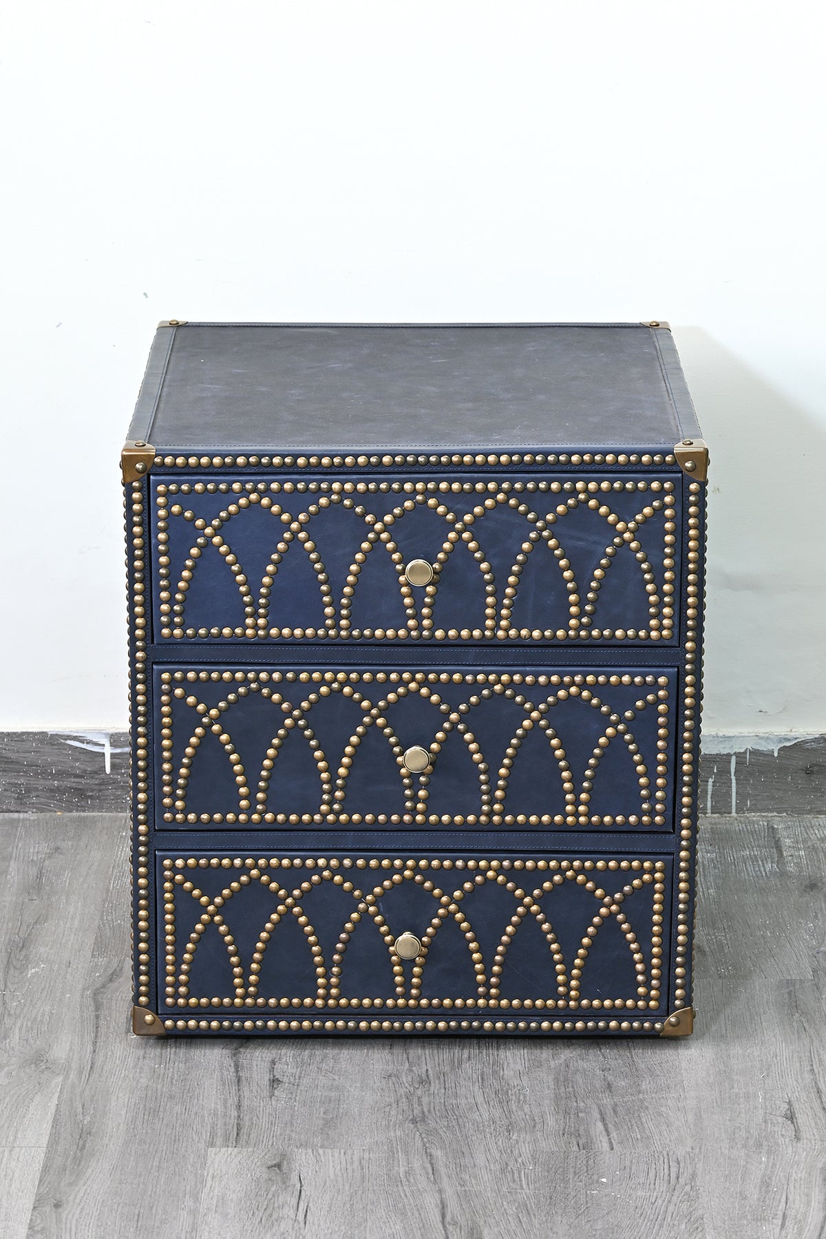 Samode leather bedside chest from a raised angle, showing the stitched leather top and three studded drawers