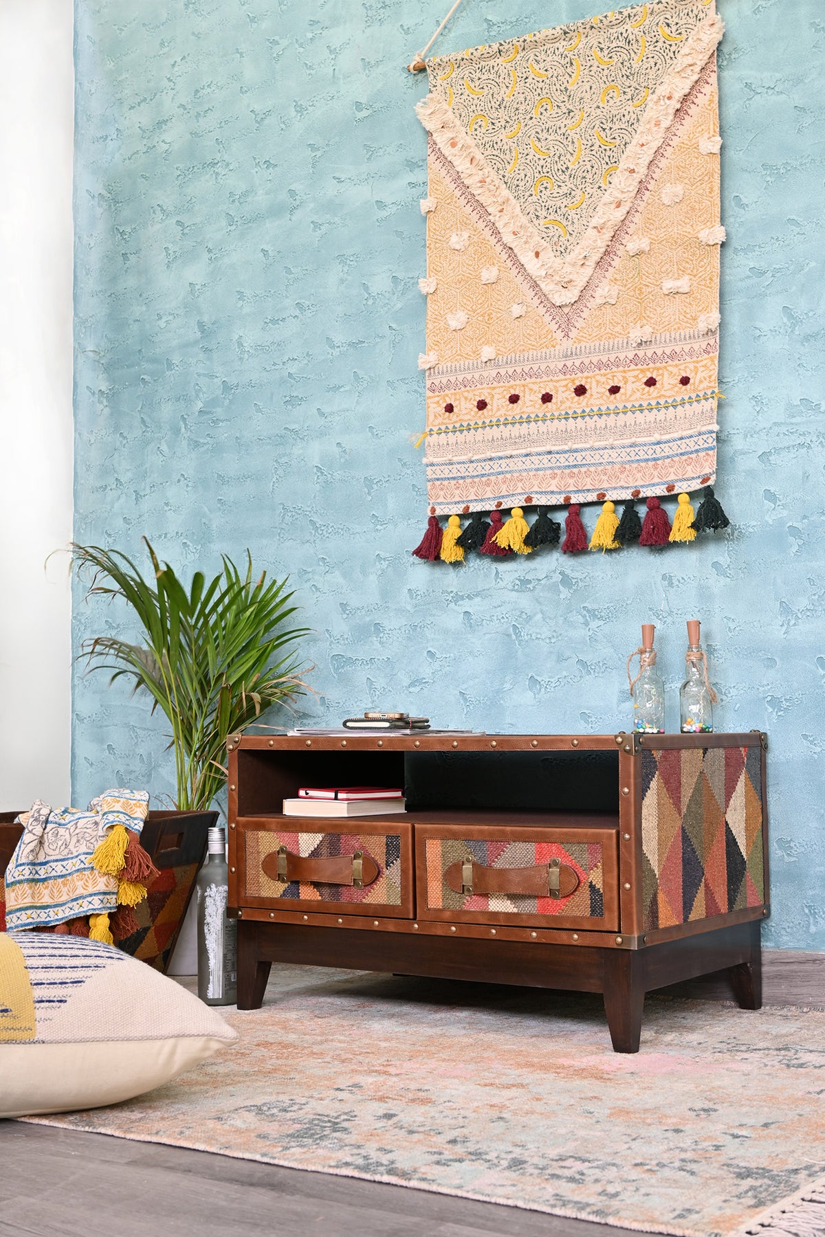 Barmer kilim and leather TV unit styled against a blue wall with a plant, floor cushions and a rug