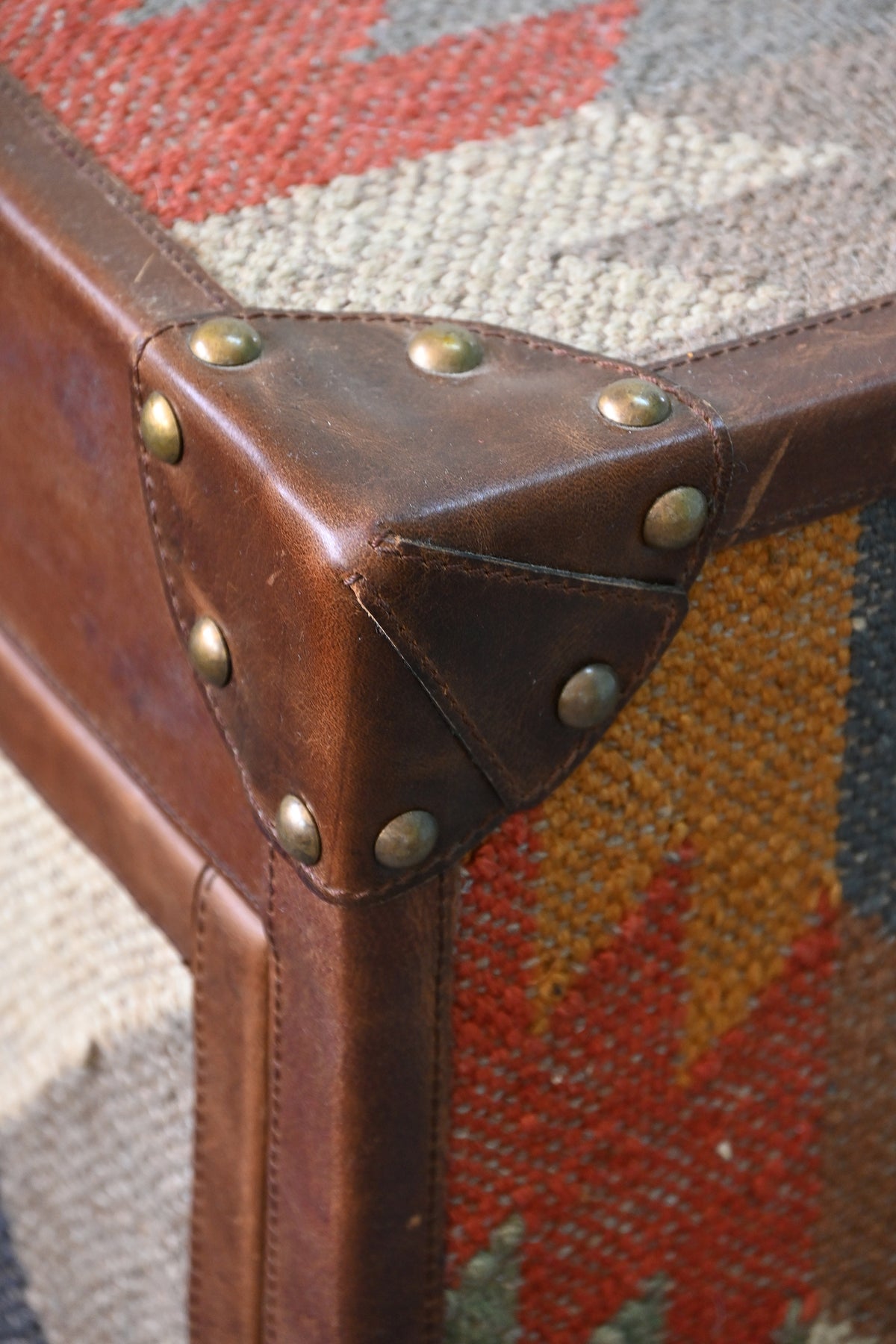 Stitched leather corner cap with brass domed studs where the kilim top meets the side — Nimaj sideboard, Art Avenue