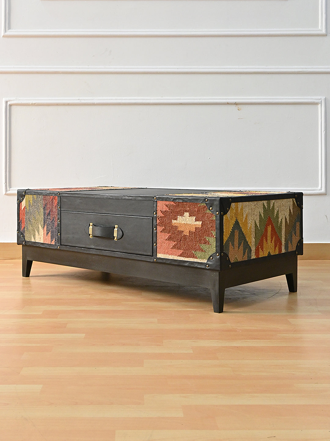Kumbhalgarh coffee table at a three-quarter angle showing the kilim-wrapped short end and brass-studded black leather binding