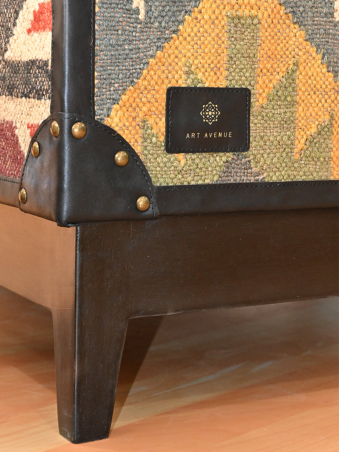 Art Avenue leather maker's tag on the kilim short end, above a studded corner cap and a tapered solid wood leg