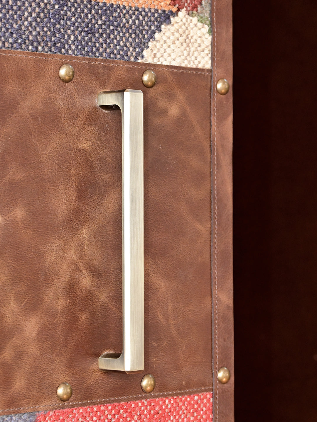 Detail of a brushed-brass bar pull on a stitched leather panel with domed brass studs, Alsisar wardrobe