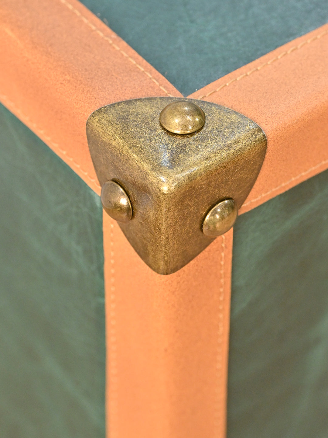 Close-up of a cast antique brass corner cap where three stitched tan leather edge bindings meet