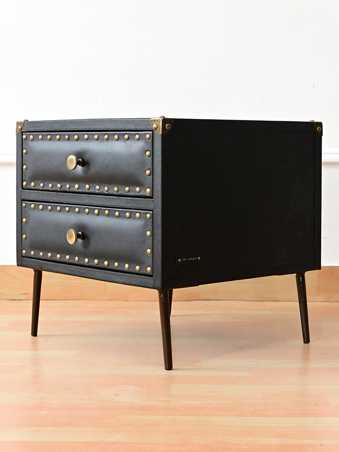 Three-quarter view of Kishangarh bedside table in Onyx leather, riveted maker's tag and dark bronze tapered legs, Art Avenue