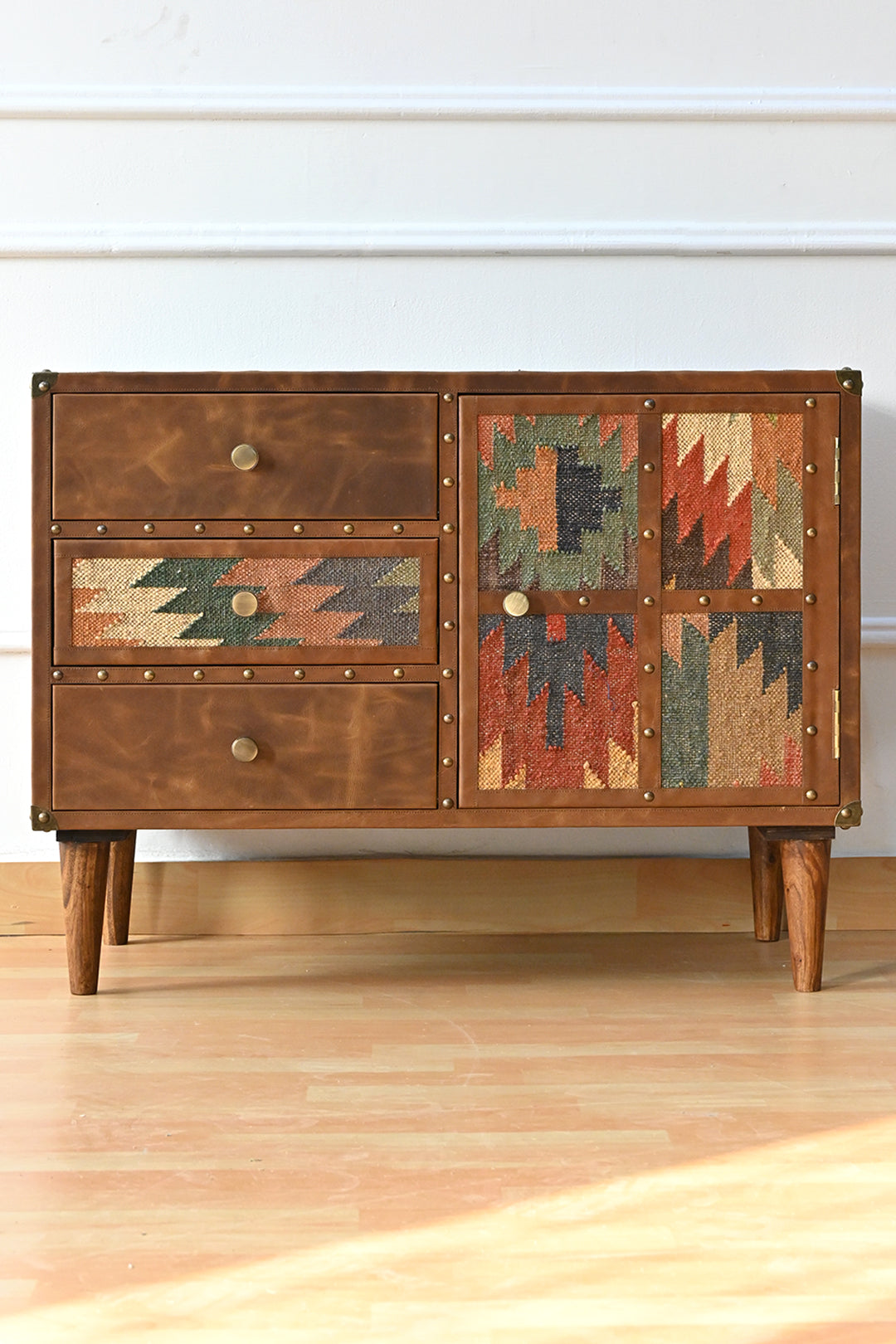 Front view of the Kanota sideboard by Art Avenue, leather and kilim drawers beside a four-panel kilim door on tapered wooden legs