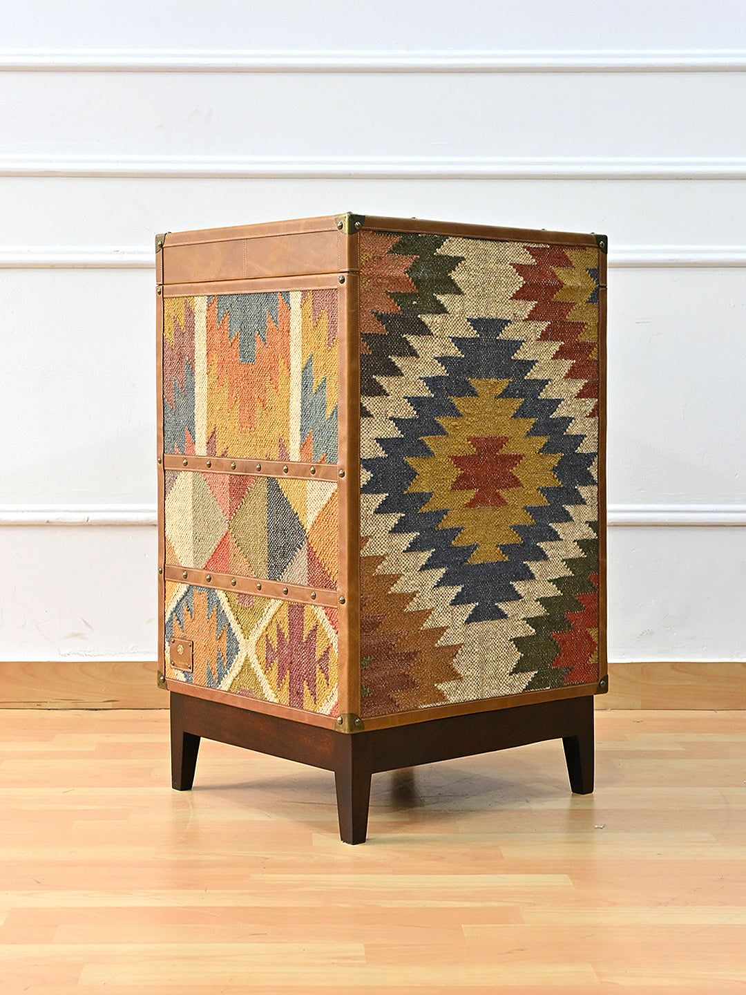 Rear three-quarter of the Osian trunk showing vintage kilim across two full faces, banded with studded leather straps. Art Avenue, made to order.
