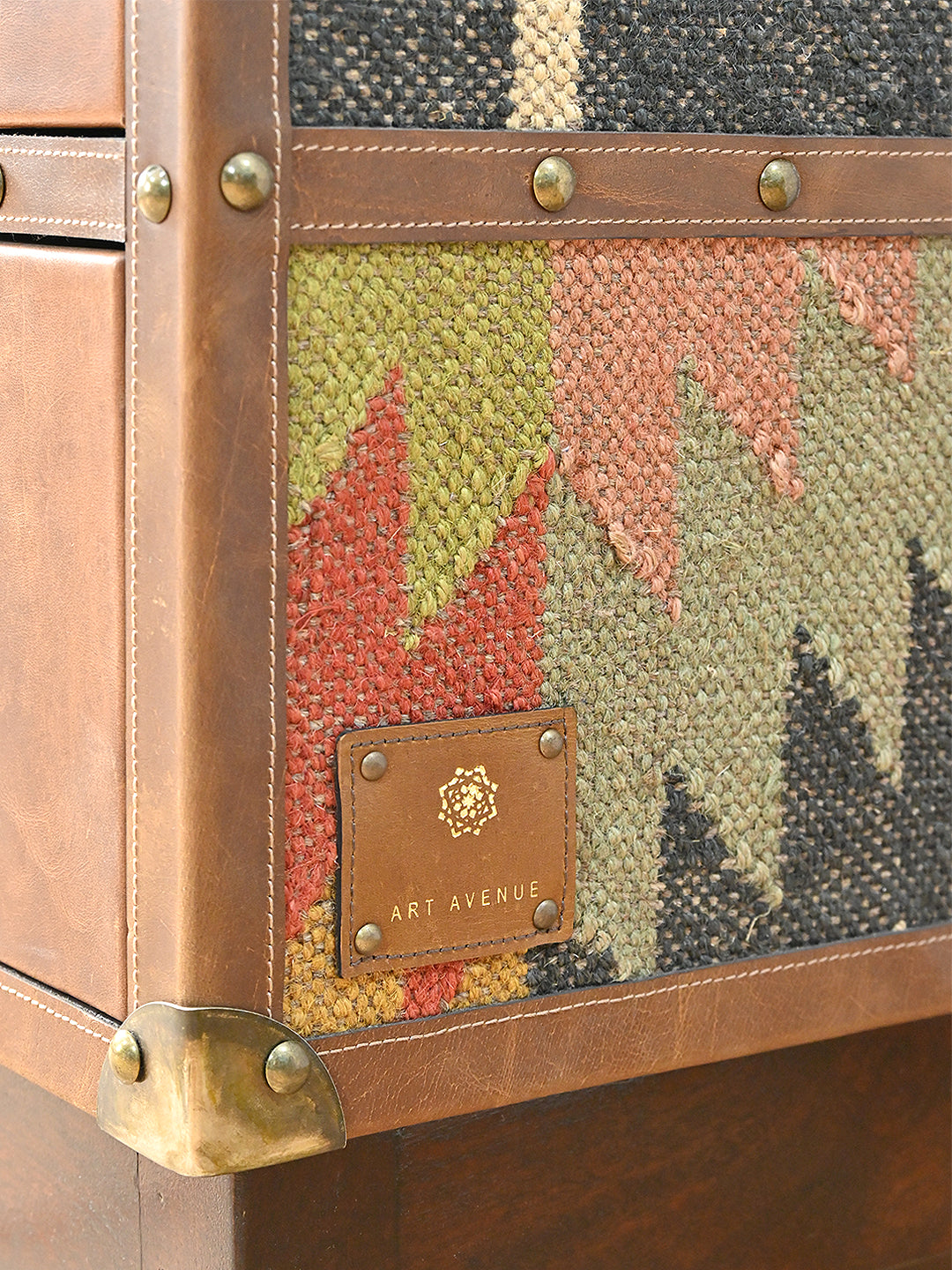 Hand-set Art Avenue leather patch on the kilim flank of the Shalimar cabinet, beside a brass corner cap