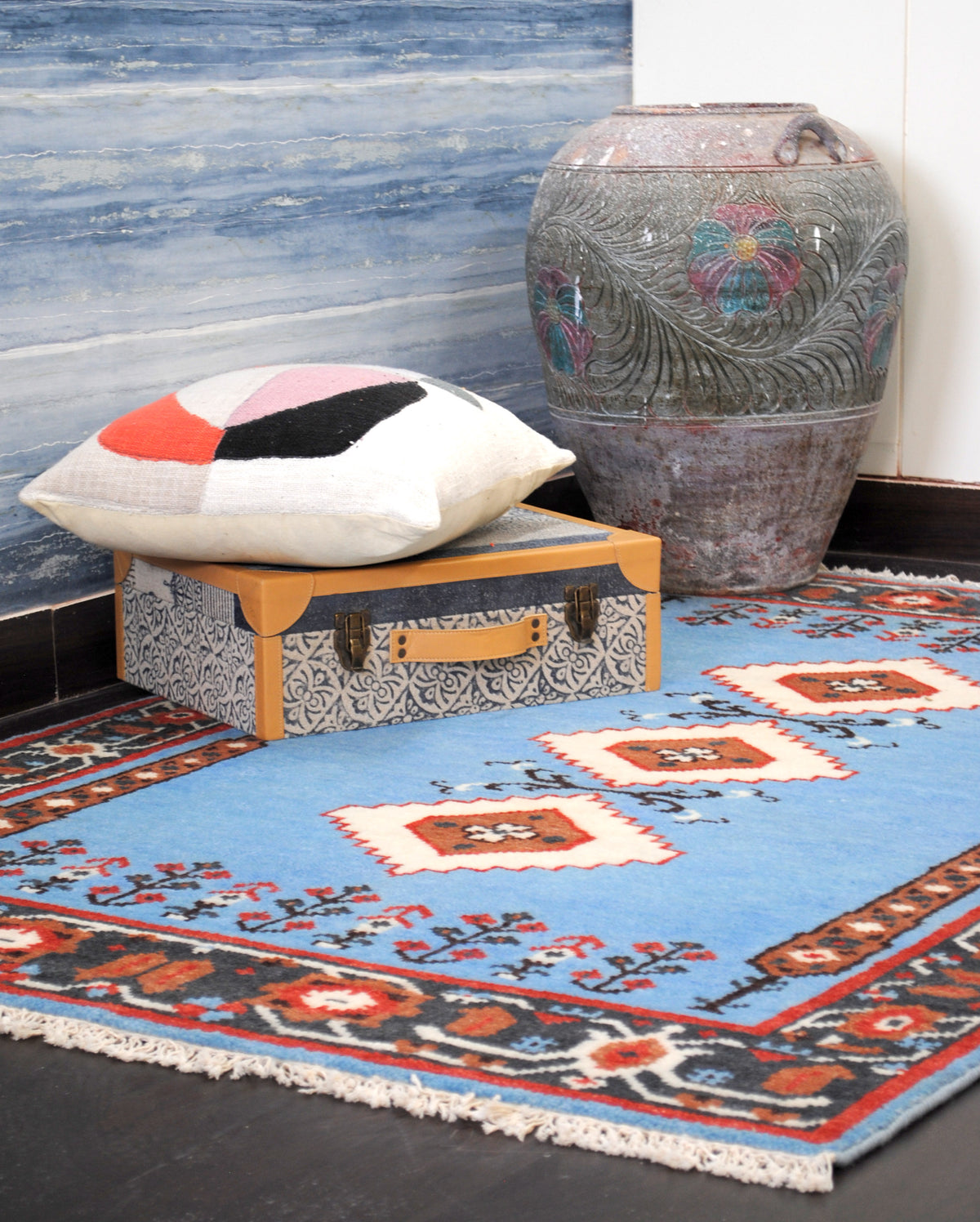 Nilgiri hand-knotted wool rug styled in a corner with a carved clay urn, a block-print trunk and a cushion, Art Avenue