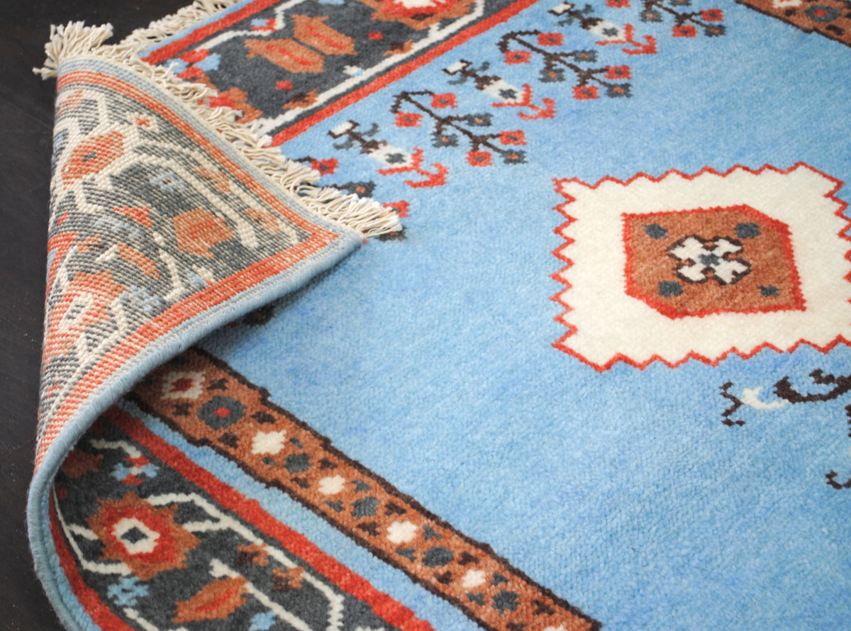 Close view of the Nilgiri rug's wool pile with an ivory medallion and rust column motif, one corner folded to show the reverse, Art Avenue