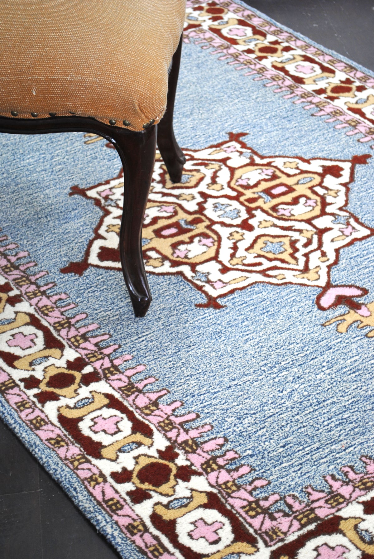 Lucknow hand-tufted wool rug styled beneath a chair, showing the denim-blue field, star medallion and ivory border, Art Avenue