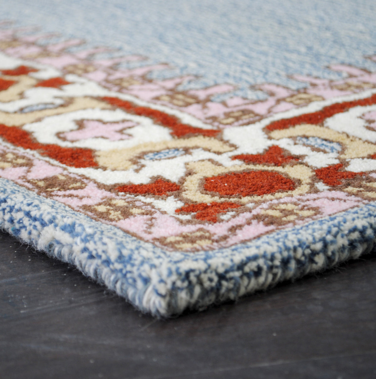 Edge of the Lucknow hand-tufted rug, showing the comb-toothed rose-pink guard and the depth of the sheared wool pile, Art Avenue