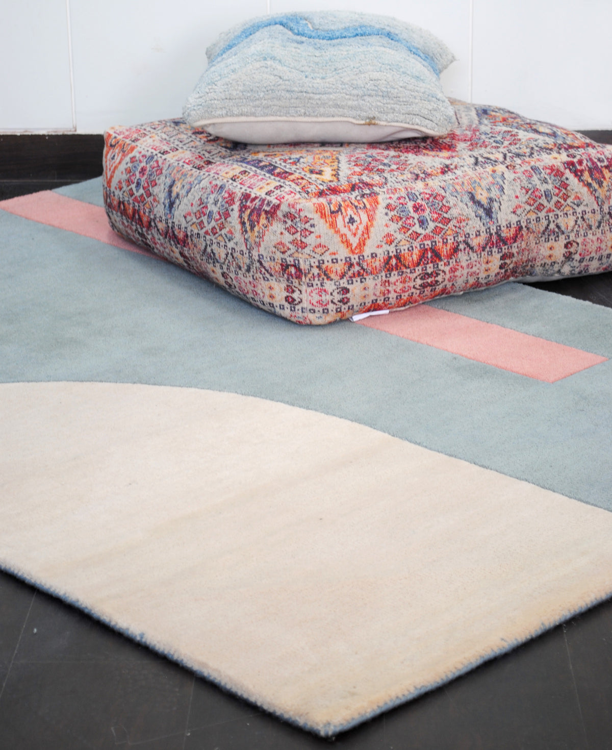 Pondicherry hand-tufted wool rug styled with a floor cushion, looking along the ivory arch towards the coral bar on the sea-glass blue field, Art Avenue