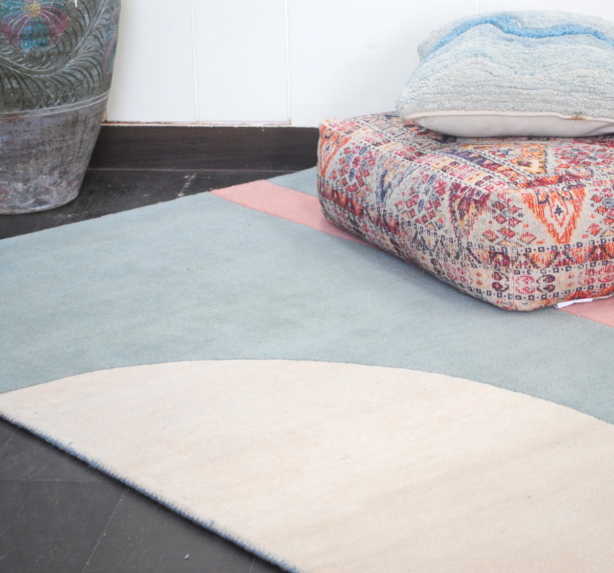 Pondicherry hand-tufted wool rug at floor level beside a carved planter, the ivory arch sweeping across the sea-glass blue field towards the coral bar, Art Avenue