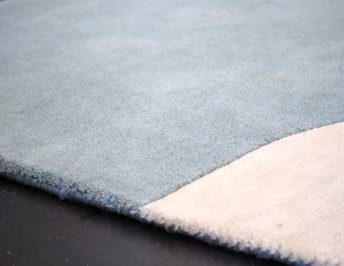 Edge of the Pondicherry hand-tufted rug, showing the blue wool binding along the sea-glass blue field and the ivory arch, Art Avenue