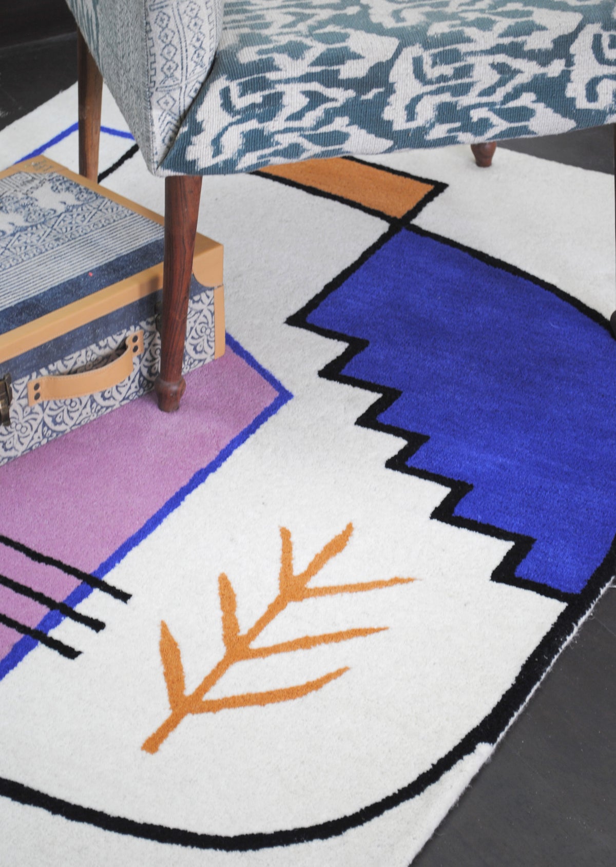 Hampi hand-tufted wool rug from above, the cobalt stepped form outlined in black beside the ochre sprig and lilac gable on an ivory ground, Art Avenue
