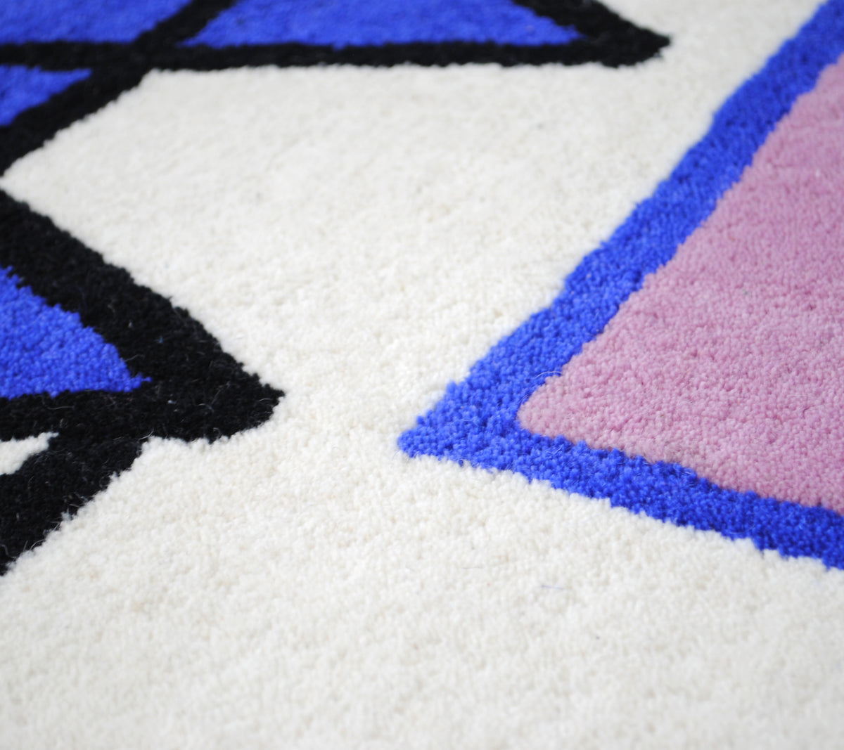 Close-up of the Hampi rug's dense cut wool pile where black, cobalt and lilac meet the ivory ground, hand-tufted New Zealand wool, Art Avenue