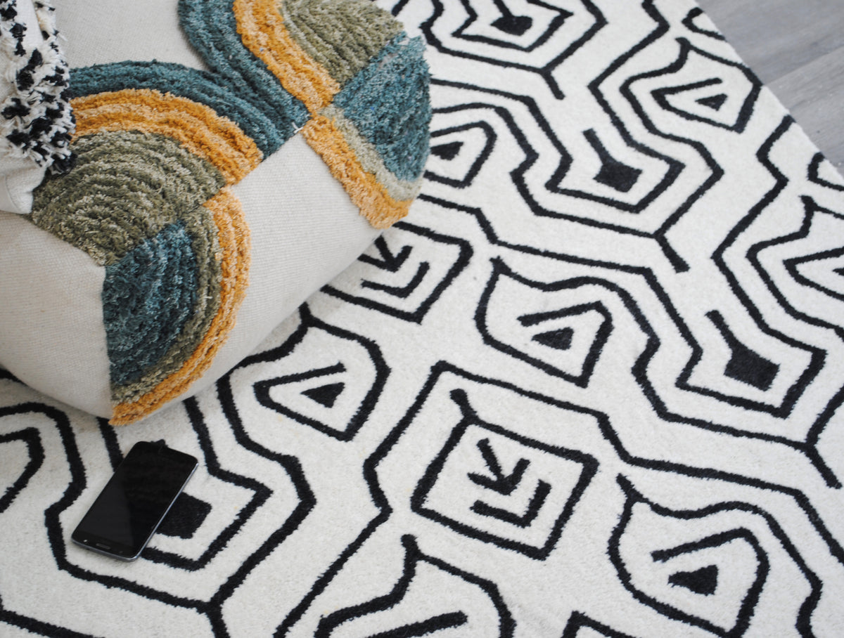 Chettinad hand-tufted wool rug from above with a tufted floor pouf resting on it, the black lattice crisp against the ivory pile, Art Avenue