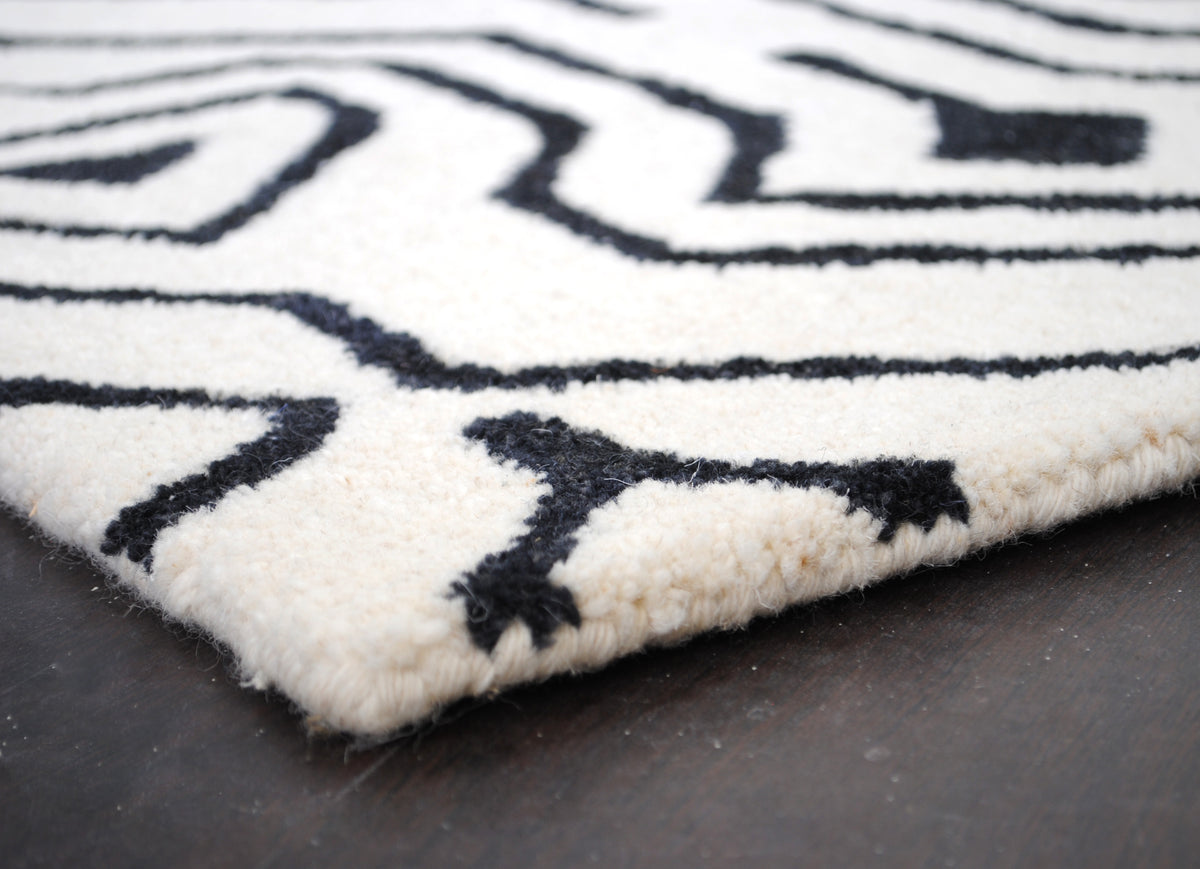 Low view across the corner of the Chettinad hand-tufted rug, showing the dense cut New Zealand wool pile and the wool-bound edge, Art Avenue