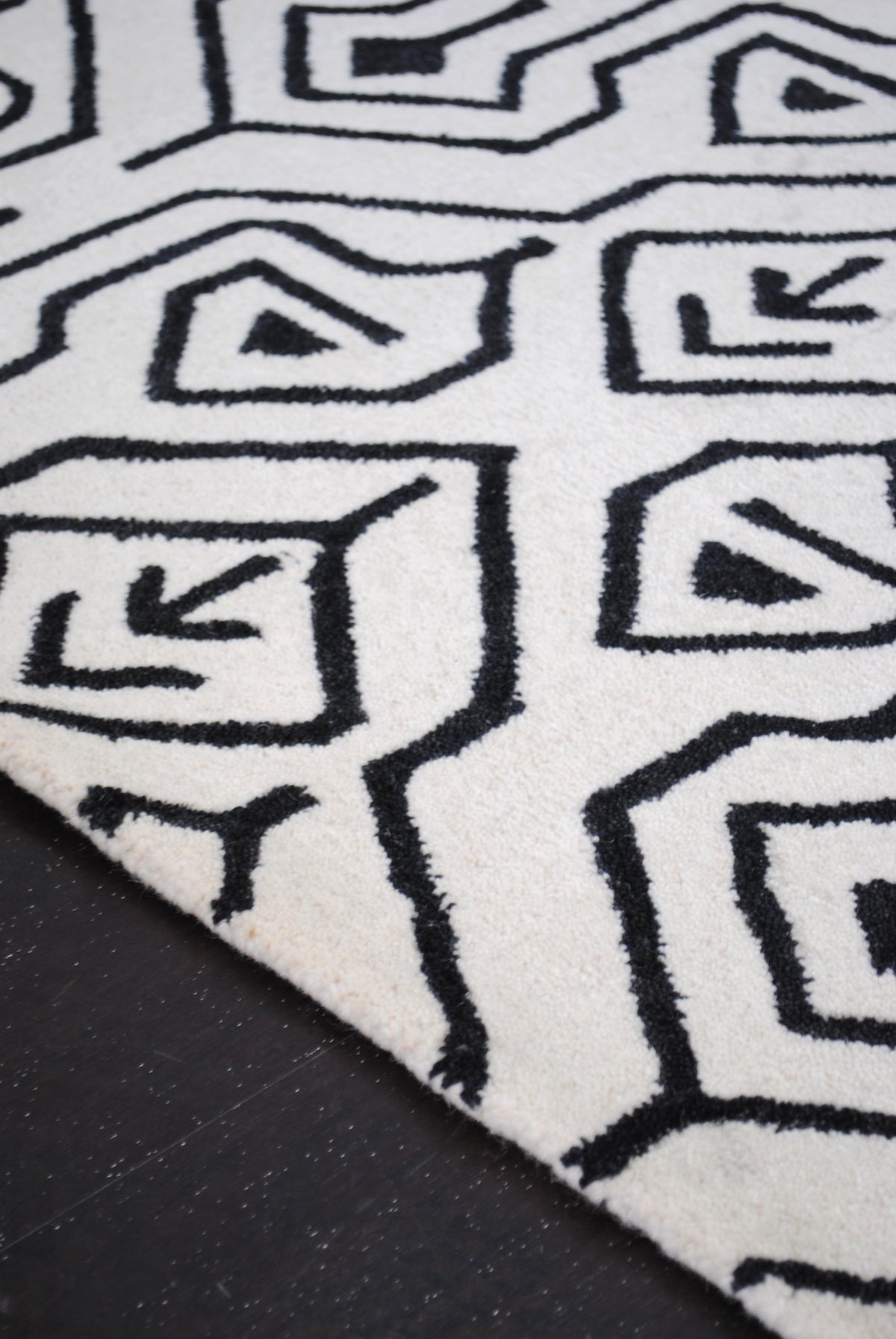 Close view of the Chettinad rug's tufted black line work, keyhole arches holding a small triangle and a feathered arrow on the ivory wool ground, Art Avenue