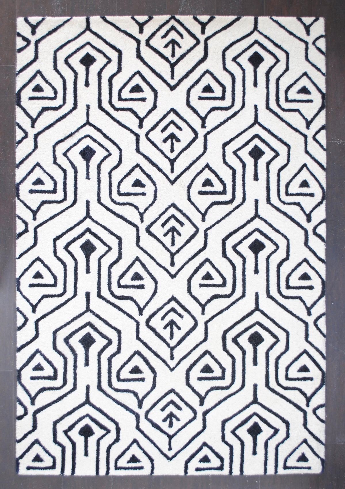 Chettinad hand-tufted wool rug laid flat on a dark wood floor, the black keyhole-arch lattice running the full length of the ivory ground, Art Avenue