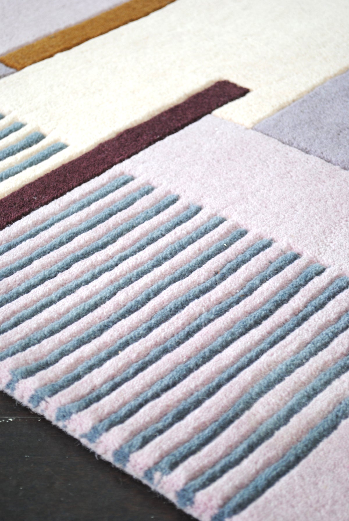 Close view of the Mumbai rug's carved stripes, dusty teal ribs standing proud of the pale pink wool pile beside an aubergine bar, Art Avenue