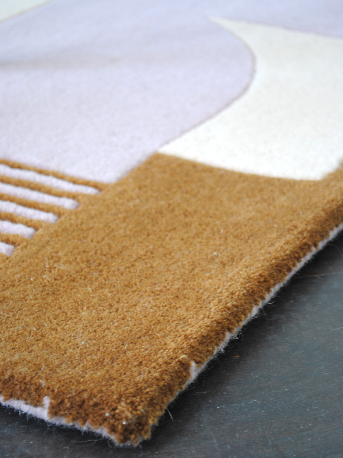 Corner of the Mumbai hand-tufted rug, showing the dense cut ochre New Zealand wool pile, carved lilac lines and the bound edge, Art Avenue