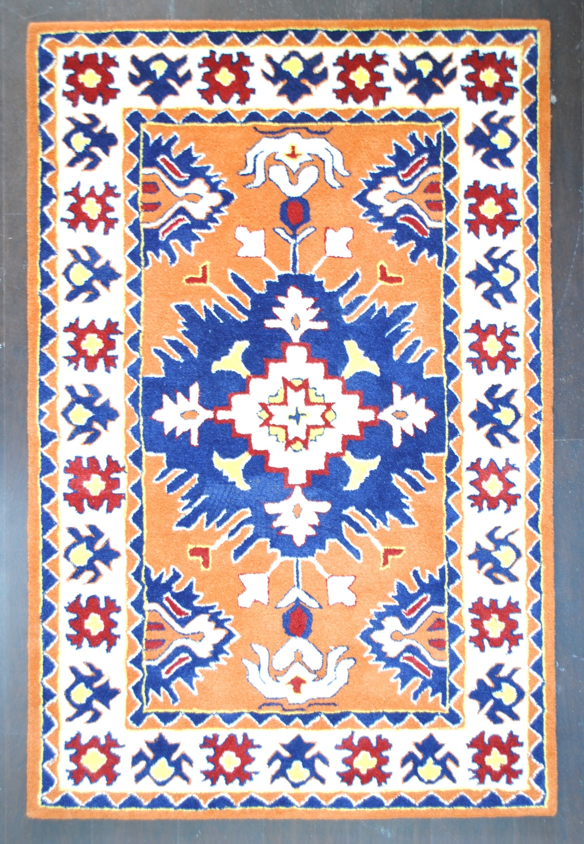 Kutch hand-tufted rug in 100% New Zealand wool, full overhead view: a stepped ivory star in a flaring navy medallion on a saffron field, framed by an ivory border of red and indigo flowers, Art Avenue, 4×6 ft